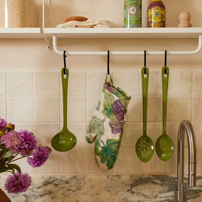 Kitchen scene with green utensils and a figgy green quilted linen oven mitt hanging above a marble counter.