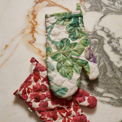 Two patterned oven mitts, one with figgy green quilted linen oven mitt and the other with red flowers, on a marble surface.
