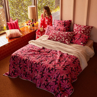 Woman sitting beside Bed with pink floral quilted throw, pink floral cushion, and pillow with pink floral pillowcase