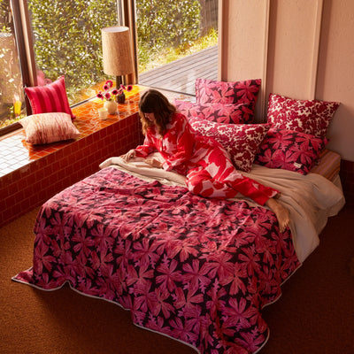 Woman lying in the bed with pink floral quilted throw, pink floral cushion, and pillow with pink floral pillowcase