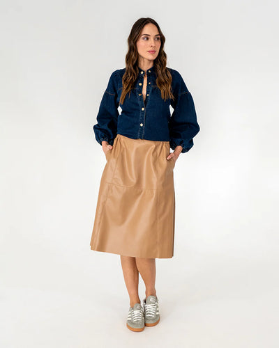 Woman wearing long sleeve top in dark blue denim and copper row skirt in tan