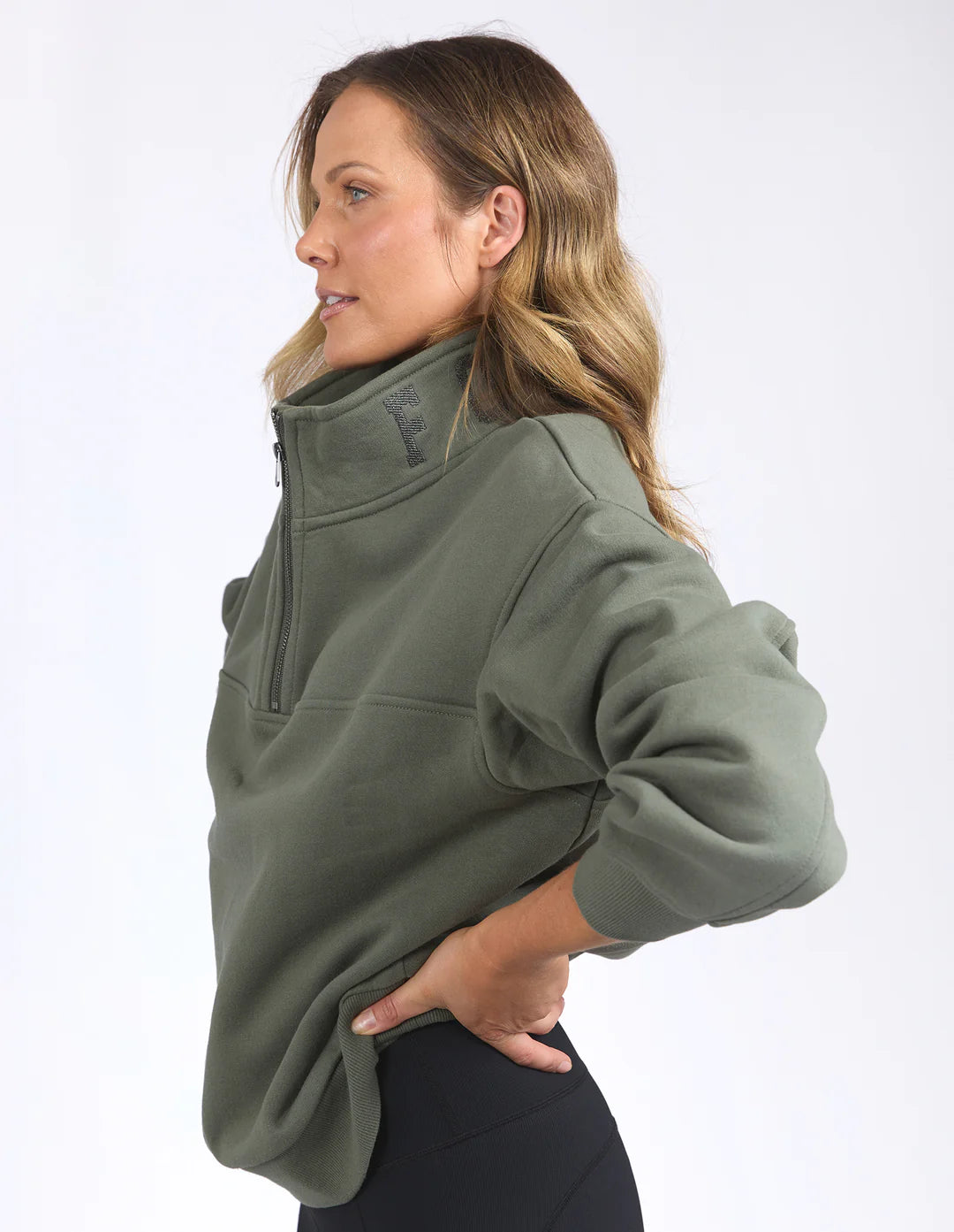 Woman facing the side wearing college zip crew khaki and black leggings