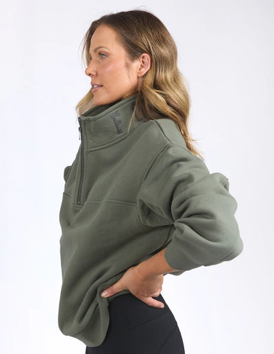 Woman facing the side wearing college zip crew khaki and black leggings