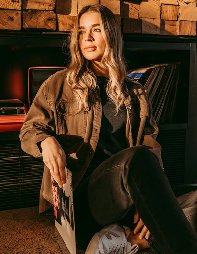 Woman seating wearing black top and pants with Daisy Overshirt - Chocolate