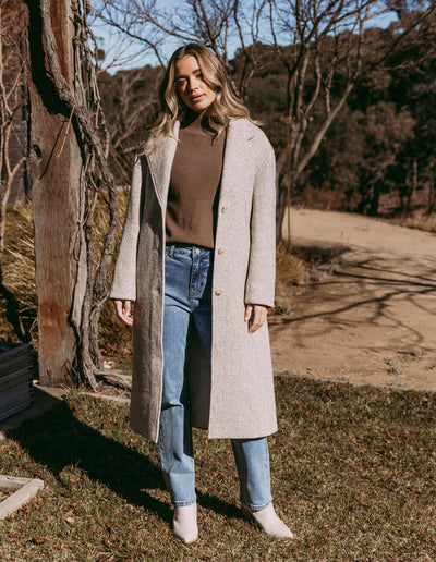 Woman standing in front f some trees wearing brown top and light blue denim pants with Whistler Coat - Oat
