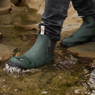 Person wearing Bobbie Ankle boot in Forest Green standing in a shallow stream.