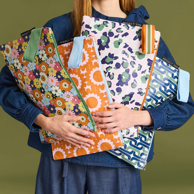 Person holding different colorful patterned zip pouch against a green background