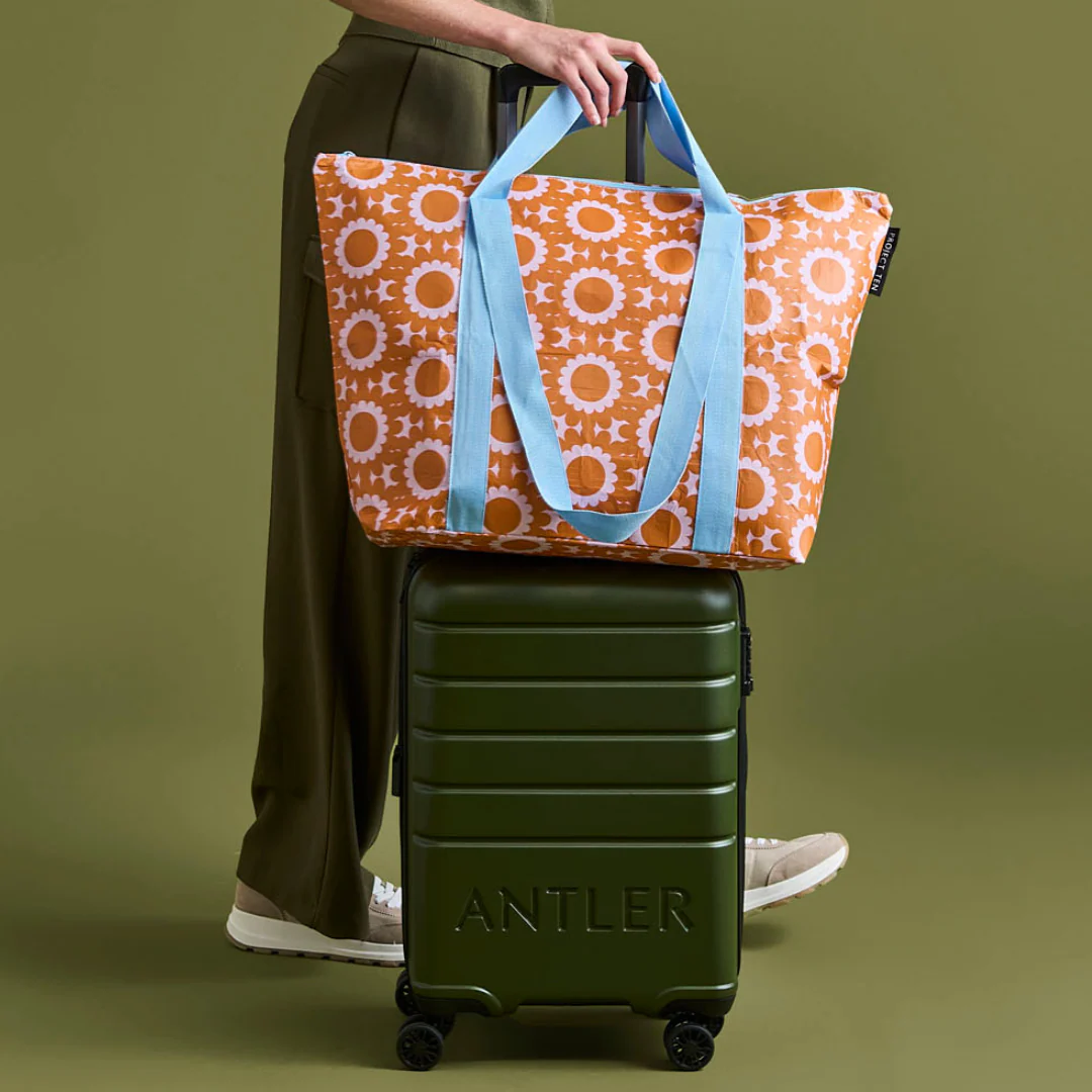 Person holding a zip medium tote bag in geo floral over a green suitcase with 'ANTLER' branding on a green background