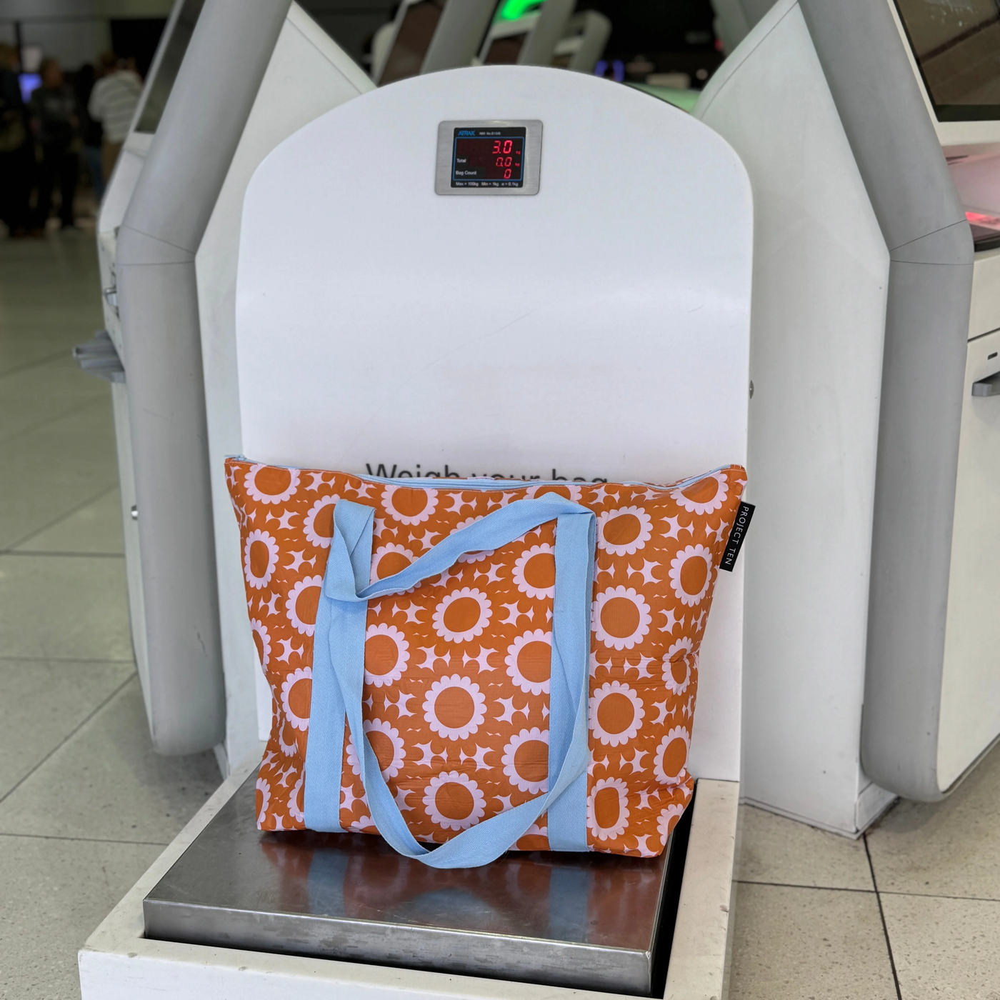 zip medium tote bag in geo floral on a luggage scale at an airport.