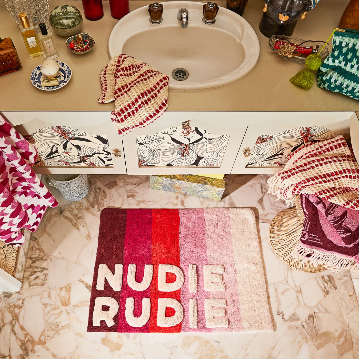 colourful bathroom with a striped mat that says “NUDIE RUDIE.” The sink area has fun patterns, and towels