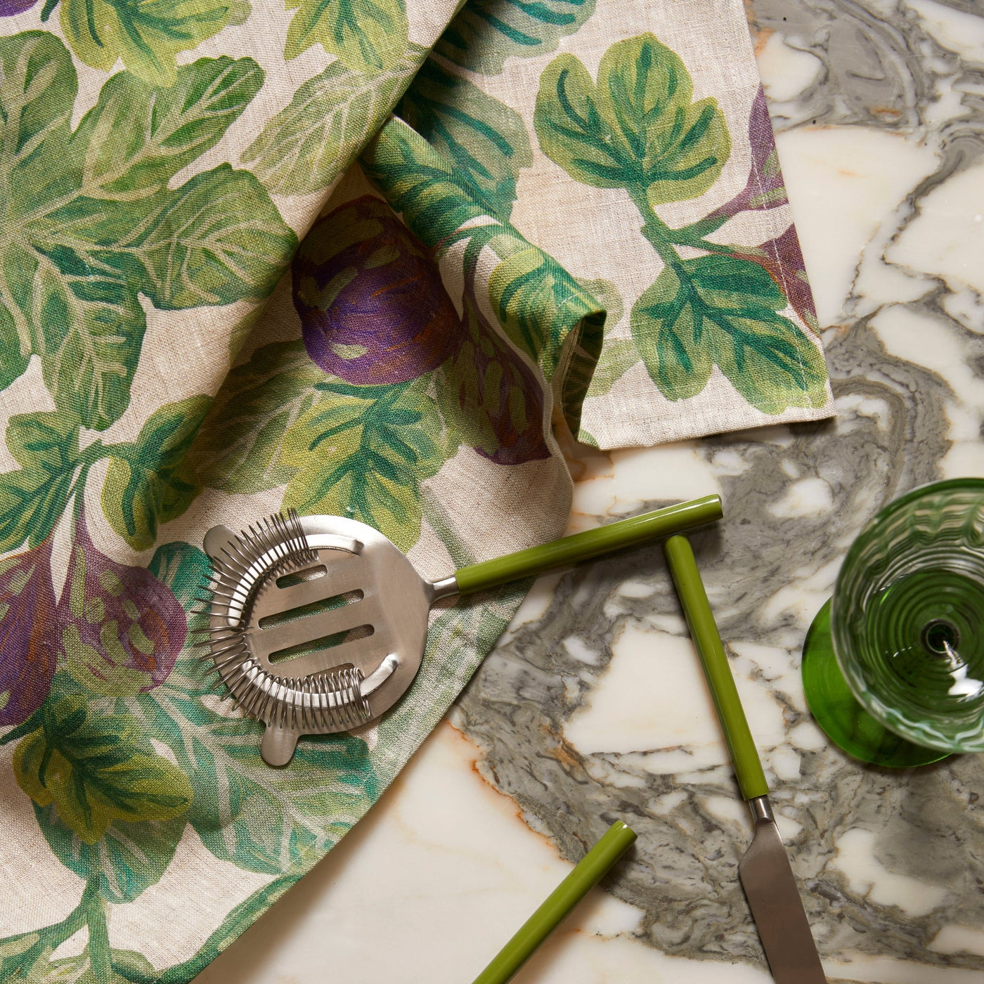 figgy green tea towel hanging with mint green utensils above a marble countertop.