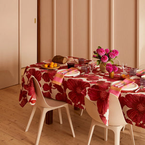 Dining table set with a red floral tablecloth, pink napkins, and a vase of bright pink flowers.