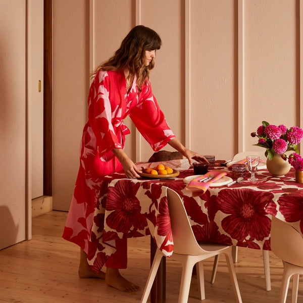 Woman in a red robe setting a table with a red floral tablecloth and leon cerise napkins set of four