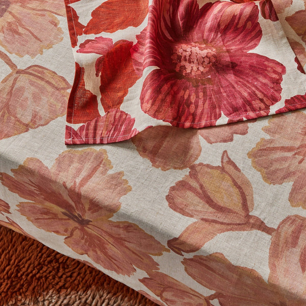 Close-up of layered floral tablecloths in red and soft pink tones, leon ceris linen napkins on a textured rug.