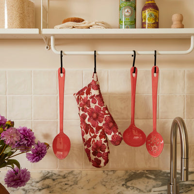 Leon cerise oven mitt and pink kitchen utensils hanging above a marble counter in a tiled kitchen.