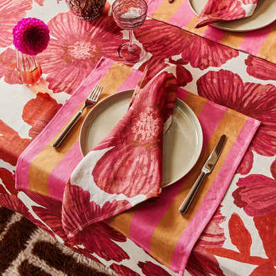 Place setting with pink and orange napkins on a red floral tablecloth.