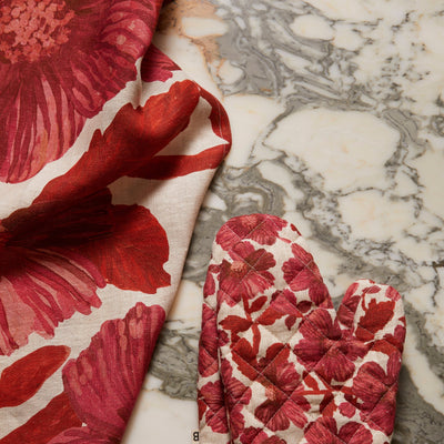 Leon cerise tea towel and leon cerise quilted linen oven mitt on a marble countertop.