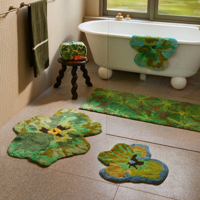 Bathroom featuring a white freestanding bathtub, pansy bath, viola small green bath mat, and mave khaki long bath mats and a matching green toiletry bag on a dark wooden stool.