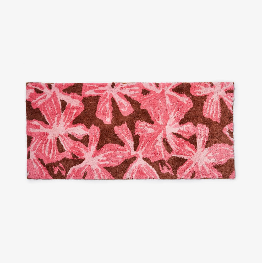 mave pink bath mats placed on a tiled bathroom floor in front of a wooden vanity with a floral toiletry bag and perfume bottle.