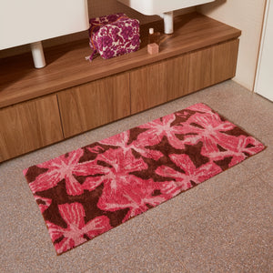 mave pink bath mats placed on a tiled bathroom floor in front of a wooden vanity with a floral toiletry bag and perfume bottle.