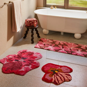 Bathroom with a white freestanding bathtub, pansy, viola small pink, and mave pink bath mats on the floor