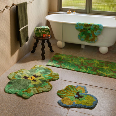Bathroom featuring a white freestanding bathtub, pansy green bath mat, viola green small bath mat , mave khaki long bath mat, and a matching green toiletry bag on a dark wooden stool.