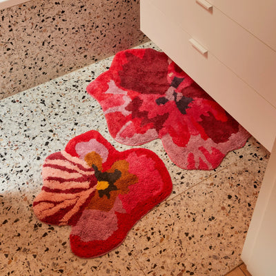 viola pink small bath mat and pansy bath mat placed on terrazzo bathroom floor next to a white cabinet with drawers.