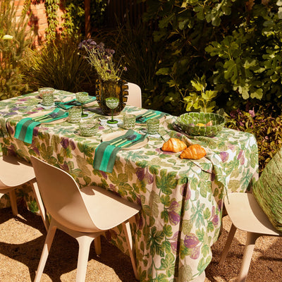 Outdoor table set with green glassware, croissants, and a fig-patterned tablecloth.