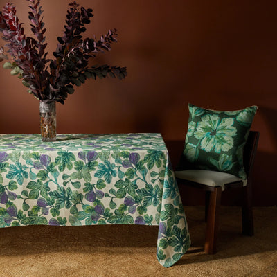 Table with a fig-patterned tablecloth, a vase with dark foliage, and a chair with a floral cushion.