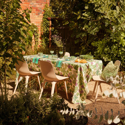 Outdoor dining setup with a fig-patterned tablecloth, green tableware, and croissants in a lush garden setting.