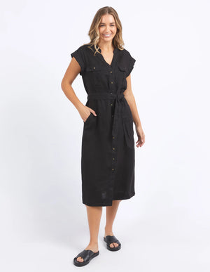 woman wearing foxwood harlow dress in black and black slip on slippers, with her hand in the dress pocket