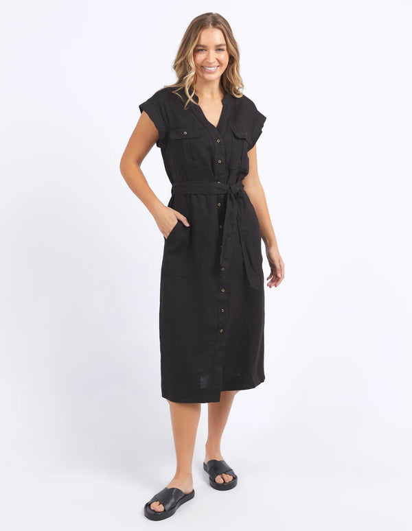 woman wearing foxwood harlow dress in black and black slip on slippers, with her hand in the dress pocket