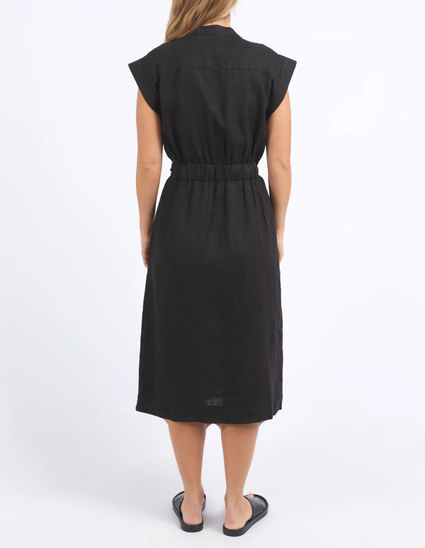 woman facing the back wearing foxwood harlow dress in black, and black slip on slipper