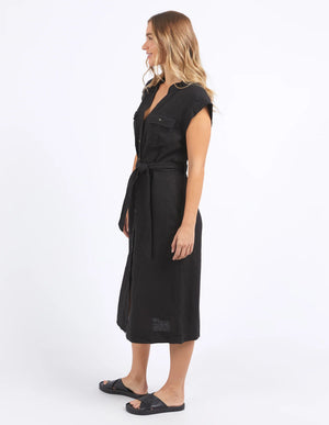 woman facing the side wearing foxwood harlow dress in black, and black slip on slippers