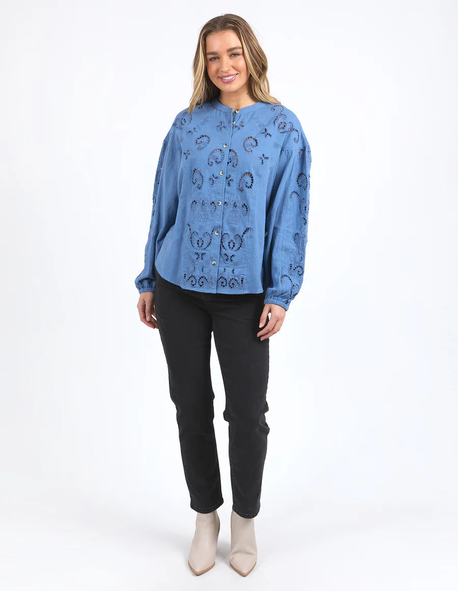 Woman wearing long sleeve blue marlow blouse, black pants and boots