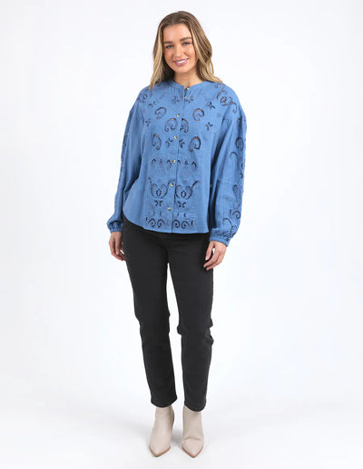 Woman wearing long sleeve blue marlow blouse, black pants and boots