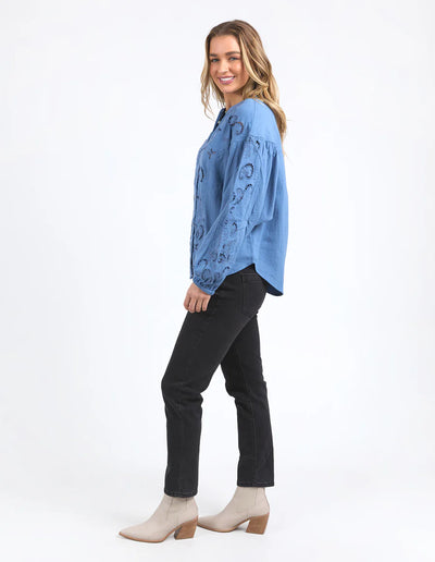 Woman wearing long sleeve blue marlow blouse, black pants, and boots