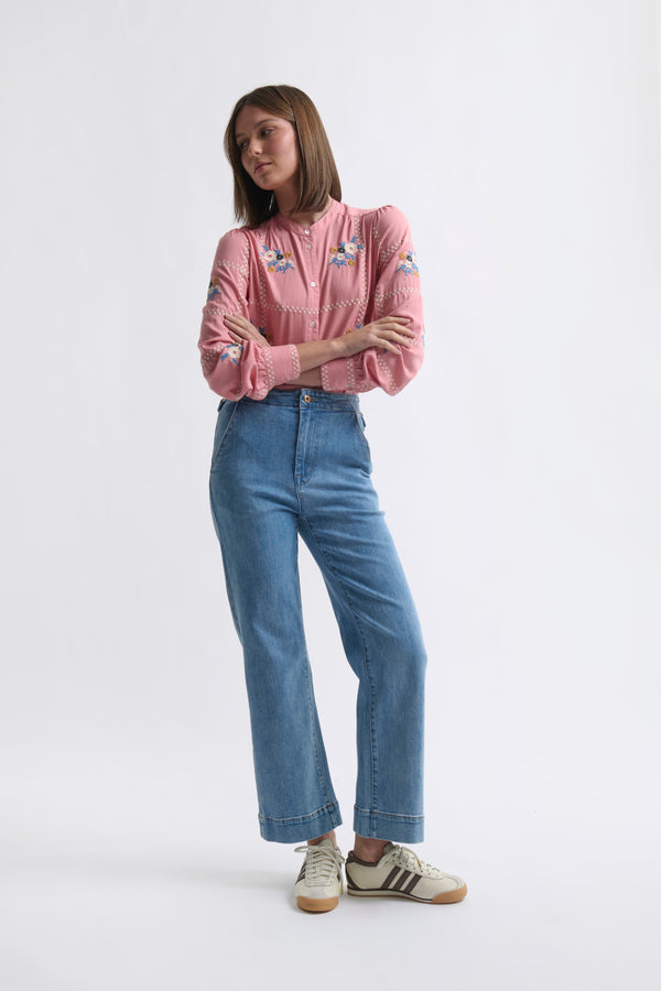Kireina Carol Shirt in Musk Pink – full-body ecom shot, model with arms crossed wearing the floral-embroidered musk pink shirt with wide-leg blue jeans and white sneakers, on a white background