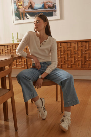 Campaign shot of Freya Jean Leather Pocket 70s Blue, model seated in styled room with warm wood backdrop