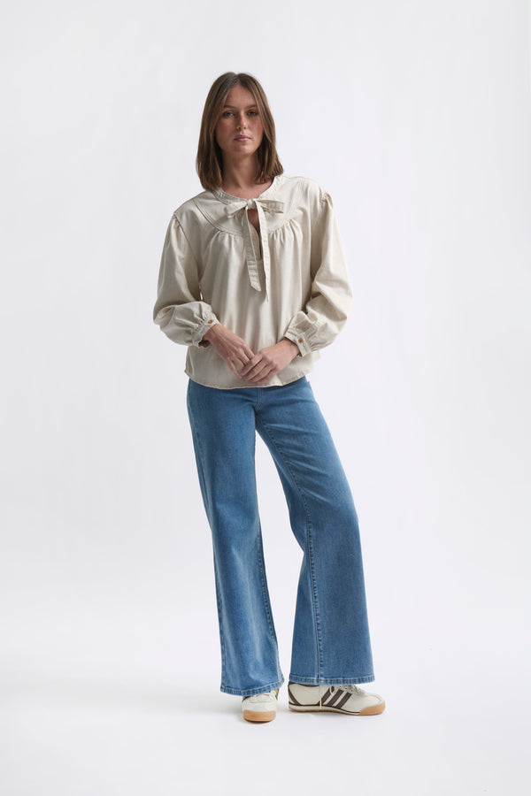 Full-length front ecom shot of Kelly Shirt Sand showing relaxed silhouette and curved hem styled with wide-leg jeans on white background