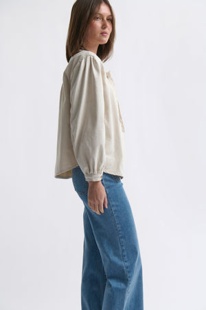 Side profile ecom shot of Kelly Shirt Sand showing puffed peasant sleeve and curved hem styled with wide-leg jeans on white background