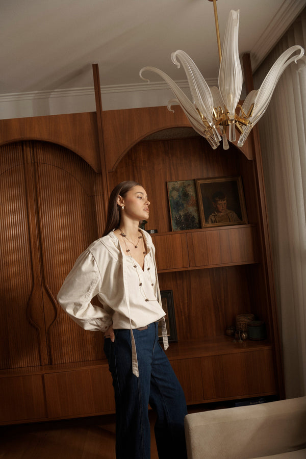 Campaign shot of Kelly Shirt Sand styled with dark jeans in elegant interior setting with wood paneling and chandelier