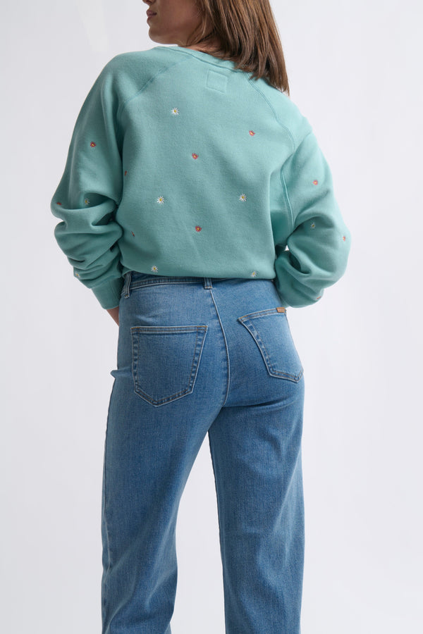 Back view ecom shot of Patti Sweatshirt Daisy Mint Green showing embroidered daisy detail across the back and ribbed collar styled with jeans on white background