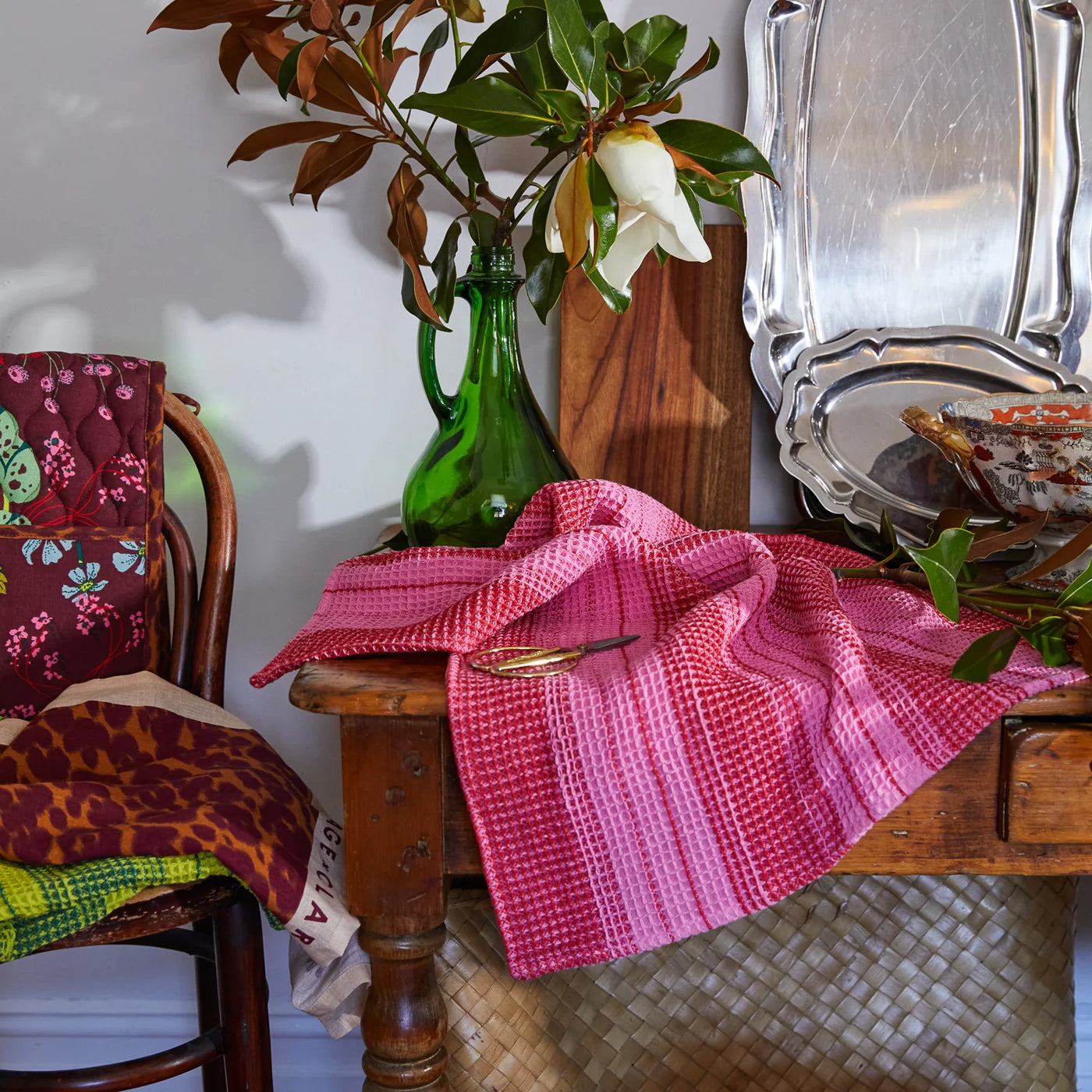 table with Brigitte Tea Towel in Cosmo Pink and scissor beside flower vase with flower