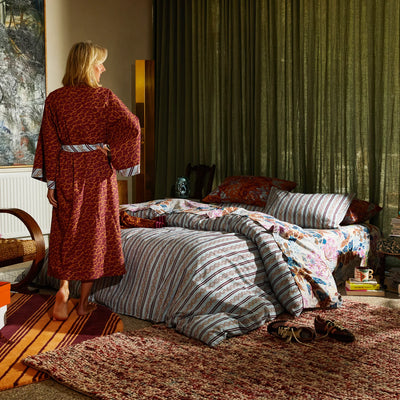 woman facing the back wearing Odette Cotton Bath Robe - Mahogany standing beside the bed